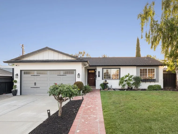 White single-story ranch home with a gray double garage, dark wood front door and a red brick walkway across a green lawn at 3749 Kersten Dr, San Jose, California